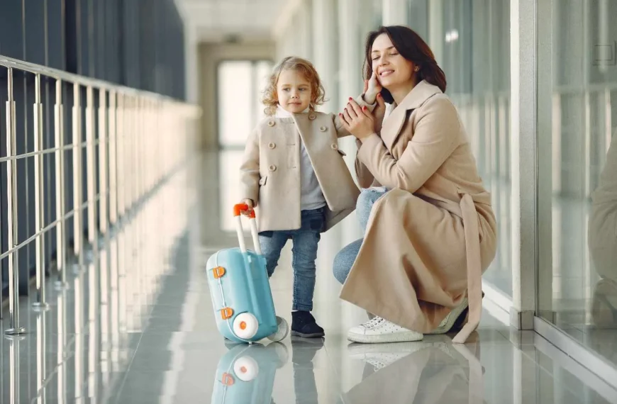 Mother and young child with a small suitcase in a hallway.
